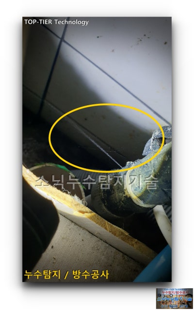 어두운 싱크대 뒤편 연결 부속에서 가는 물줄기가 뻗쳐 나오는 지점을 노란 원으로 표시한 사진
