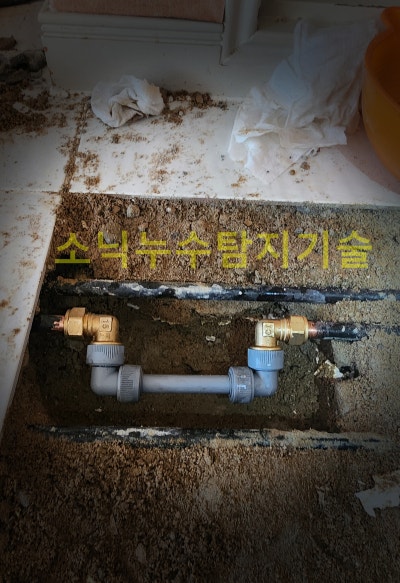 바닥을 좁게 파낸 홈 안에서 동관 난방배관을 절단하고 부속으로 이어 붙인 수리 완료 부위