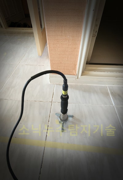 봉덕동 아파트 현관 앞 타일 바닥에 청음 탐지 센서를 올려두고 누수음을 듣는 장면