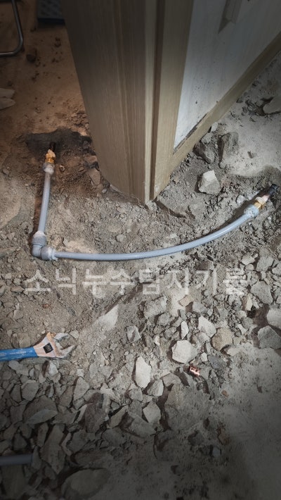 굴착한 바닥에서 방 문틀 옆을 지나가도록 새로 이은 회색 PB 난방 배관과 연결 부속