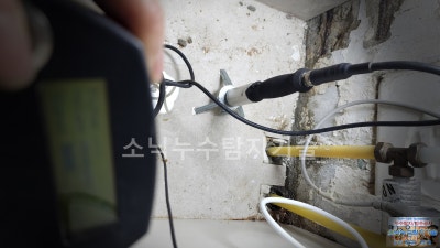 베란다 벽면 배관 옆에 청음 장비 센서를 대고 누수음을 듣는 탐지 장면