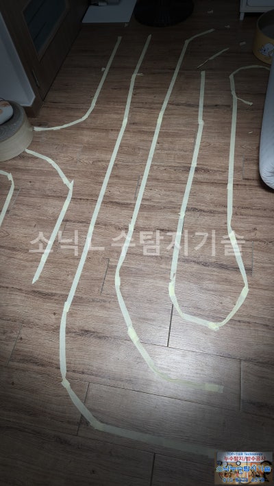 온도 차이로 파악한 난방배관이 지나가는 선을 원룸 바닥 마루 위에 테이프로 표시해 둔 모습