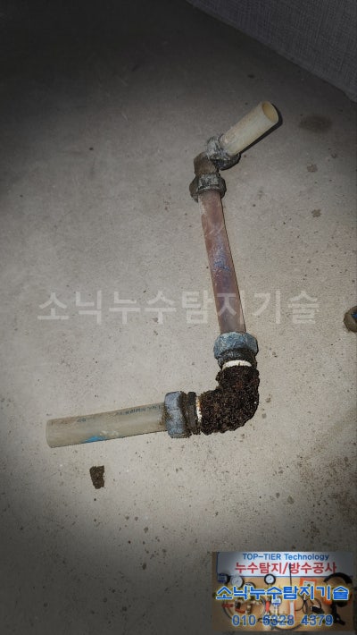 잘라낸 온수배관 조각, 아래쪽 엘보 부속에 붉은 부식물이 두껍게 엉겨 붙어 있다