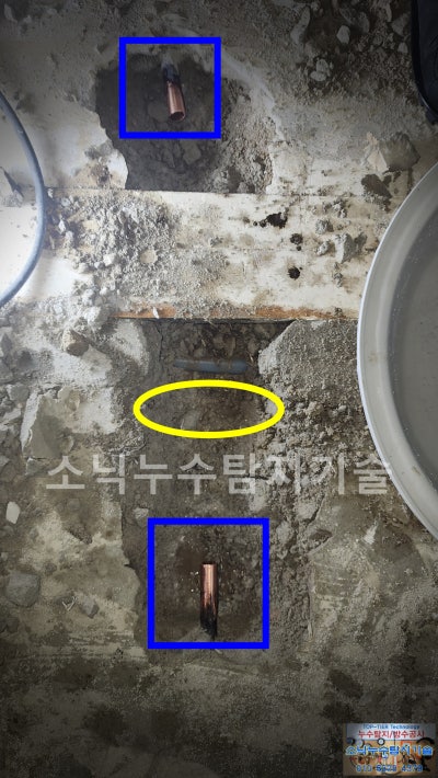문틀 경계를 사이에 두고 바닥 두 곳을 굴착해 드러낸 동관 절단면과 누수가 있던 자리를 노란 타원으로 표시한 모습